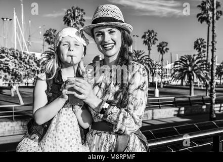 Summertime at colorful Barcelona. smiling elegant mother and daughter tourists on embankment in Barcelona, Spain drinking bright red beverage Stock Photo