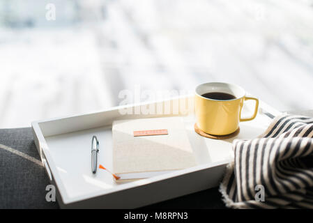 Close-up of diary between pen and coffee cup in tray on sofa Stock Photo