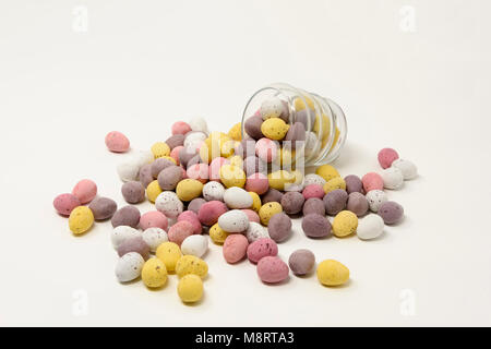 UK,  JANUARY 2018 - small brightly coloured sugar coated chocolate Easter eggs spilling out from and supporting a shaped glass cup Stock Photo