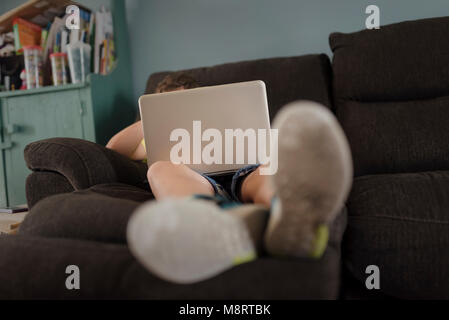 Full length of boy using laptop computer while relaxing on sofa at home Stock Photo