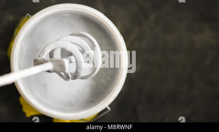 Paddle mixer over the bucket with white paint for wall, DIY tools and accessory, workflow close up, banner with copyspace