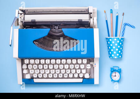 Flat lay of typewriter, office supplies and alarm clock on pastel blue background minimal creative concept. Stock Photo