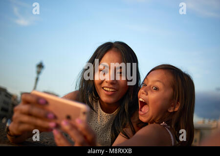 Playful mother and daughter taking selfie while standing against sky Stock Photo
