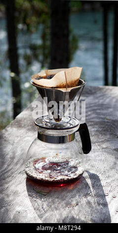 Making coffee with a drip filter holder on a rustic table near a river in summer. Stock Photo