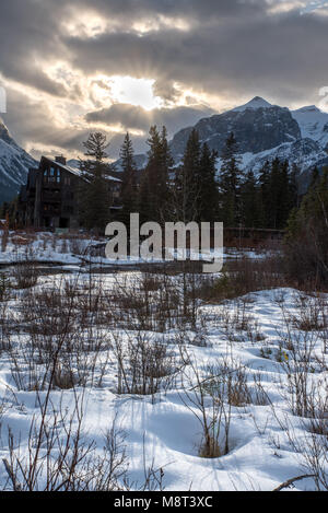 Sunset along the creek in Spring Creek, Canmore with snow, a bridge, trees, and the mountains Stock Photo