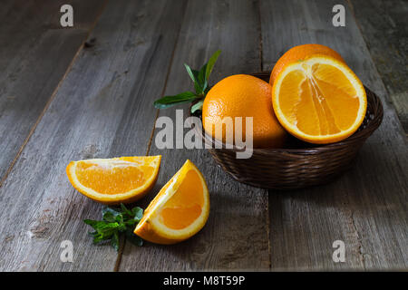 Whole and cut oranges with mint leaves close-up in a wicker basket on a wooden background. Rustic style Stock Photo
