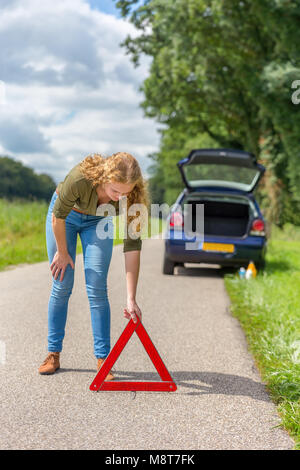 Caucasian teenage girl placing hazard warning triangle on rural road Stock Photo