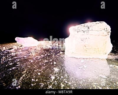 Melting pieces of chopped ice blocks. Strong colorful backlight shine deep cracks, low angle view. Far flat horizon. Stock Photo