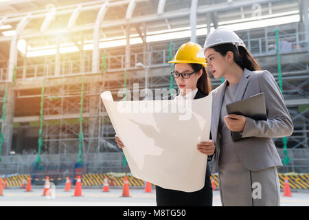 Two female engineers checking construction plan on site. Seriously staring at the blueprint of the building. Stock Photo