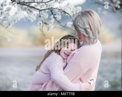 Family love and lifestyle. Portrait of mother and daughter gently embrace in the garden with flowering almendra Stock Photo