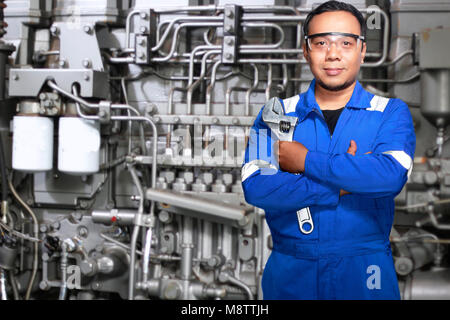 Young Asian mechanic engineer in blue uniform with arms crossed in front of industrial machine at coal mining workshop, Tenggarong, Indonesia. Stock Photo