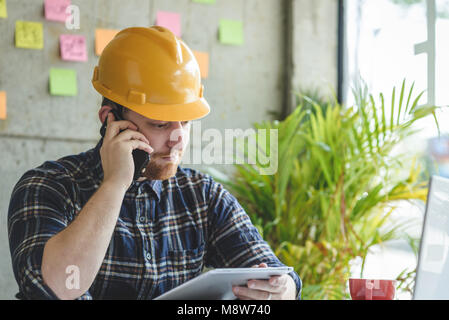 Engineer talking with phone and looking at tablet in office. Stock Photo