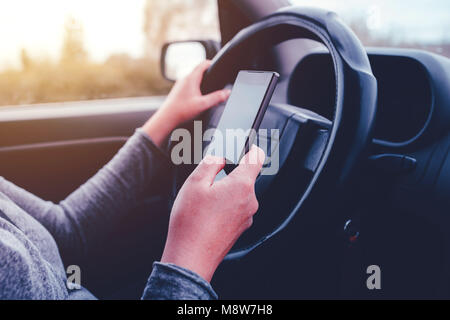Woman simultaneously driving car and reading text message, mobile smart phone in female hands over vehicle steering wheel Stock Photo