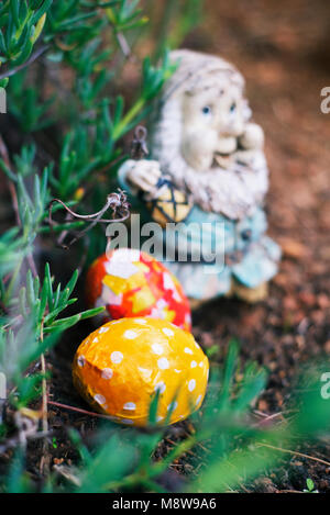 closeup of some homemade decorated easter eggs, made by myself, hidden in the garden next to an old and weathered garden gnome Stock Photo