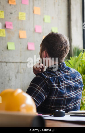 Back of engineer sitting in office and look at colorful sticky message on cement wall. Work lifestyle concept. Stock Photo