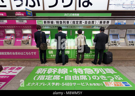 4 businessmen using 4 ticket vending machines in a Tokyo train station Stock Photo