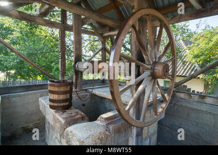 Old,traditional, wooden well with a large wheel, chain and bucket in the country side of Romania Stock Photo