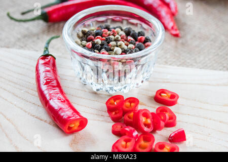 Chili pepper lies on a sackcloth on a wooden table. On the table scattered dry peppercorns Stock Photo