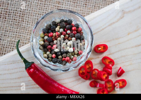 Chili pepper lies on a sackcloth on a wooden table. On the table scattered dry peppercorns Stock Photo