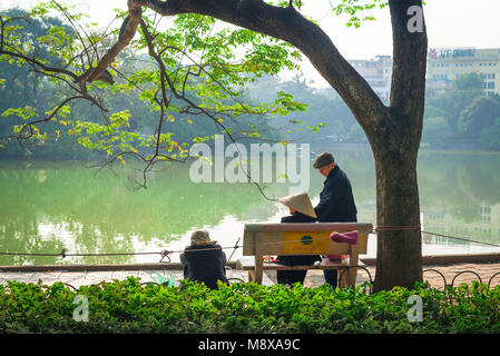 Vietnam people, rear view of elderly citizens in Hanoi enjoying spring afternoon sunshine on Hoan Kiem Lake, Vietnam. Stock Photo