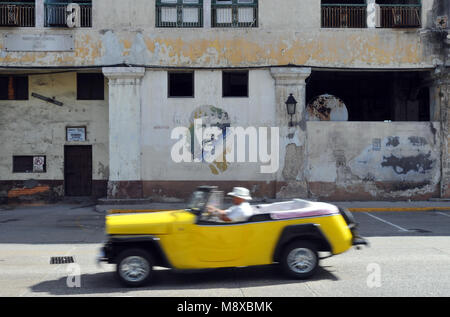 A classic car drives past street art depicting Cuban revolutionary icon Ernesto 'Che' Guevara, painted on a dilapidated building in Old Havana. Stock Photo