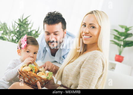 The beautiful young woman holding a wicker basket with full of tasty baked goods offering it to her husband and sweet daughter, and with a smile on th Stock Photo
