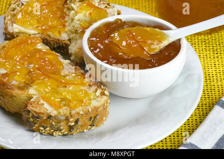 Jam made from organic oranges a marmalade in a small white dish with toast in the background on a table setting room for tex and copy space Stock Photo