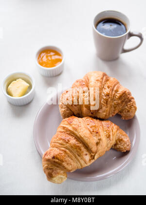 Above view of a Continental breakfast with French croissants, butter, jam and black coffee on white table Stock Photo