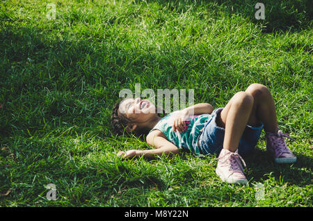 Laughing little girl lying on the grass in the park Stock Photo