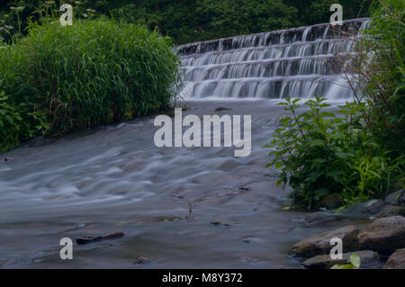 Flowing water turned milky white by a long exposure as it flows around green and brown moss covered rocks. Stock Photo