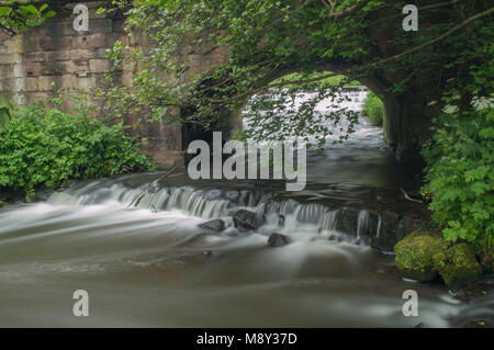 Flowing water turned milky white by a long exposure as it flows around green and brown moss covered rocks. Stock Photo