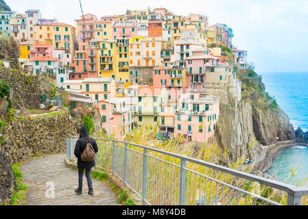 Woman walking on a path with view on the small traditional Italian village of Manarola with colorful houses now a popular tourist destination in Cinqu Stock Photo