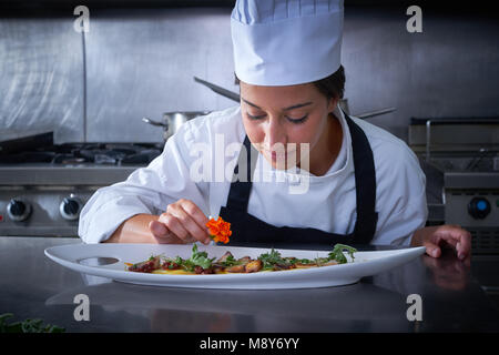 Chef woman garnishing flower in dish at stainless steel kitchen Stock Photo