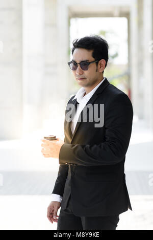 A modern businessman with coffee in his hand is walking along the building, thinking about business projects Stock Photo