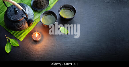 Green Tea In Iron Asian Teapot With Leaves And Bamboo Mat On Black Stone Stock Photo