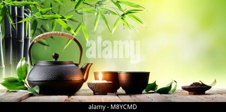 Black Iron Asian Teapot and Cups With Green Tea Leaves Stock Photo