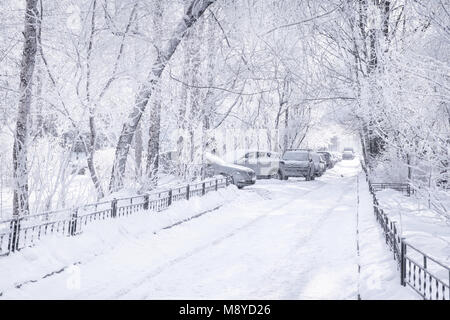 Winter city scene. White snow-covered yard with cars and empty road. High key Stock Photo