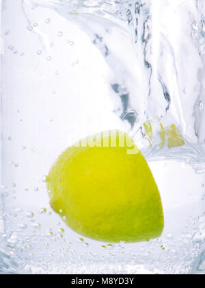 Green lime half falling into clear blue water close up Stock Photo