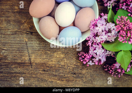 Easter background with handmade painted purple eggs and lilac on a wooden vintage board with place for text. Top view. Copy space. Stock Photo