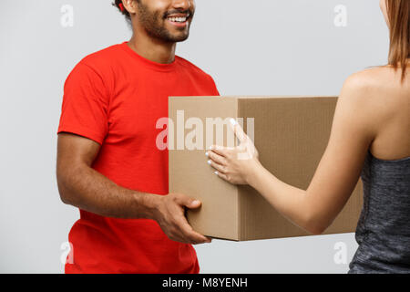Delivery Concept - Handsome African American delivery man giving  package to homeowner. Isolated on Grey studio Background. Copy Space. Stock Photo