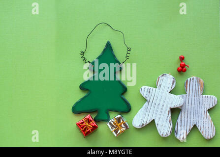 two wooden gingerbread men under  mistletoe with Christmas tree on a green background with gift under the wooden tree Stock Photo