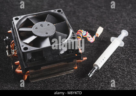 CPU heat sinker from a PC and a thermal grease. Copper heatsinker with a fan for cooling the processor. Focus on the heatsink, isolated on a dark back Stock Photo