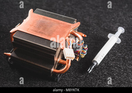 CPU heat sinker from a PC and a thermal grease. Copper heatsinker with a fan for cooling the processor. Focus on the heatsink, isolated on a dark back Stock Photo