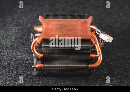 CPU heat sinker from a PC. Copper heatsinker with a fan for cooling the processor. Isolated on a dark background. Bottom view. Stock Photo