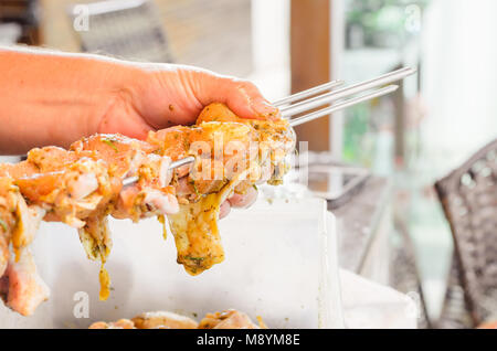 Sticking the seasoned chicken pieces on the skewer. Fresh raw chicken thighs ready for barbecue. Stock Photo