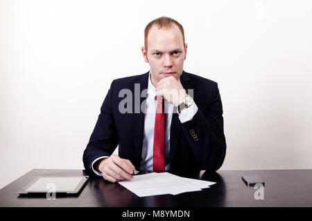 The face of plenary leadership. Thoughtful businessman in formal wear holding hand on chin while sitting at his working place, documents, phone, the t Stock Photo
