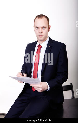 accountant holds and counts, reads paper or documents, stands at a table dressed in a classic suit in front of white background. Stock Photo