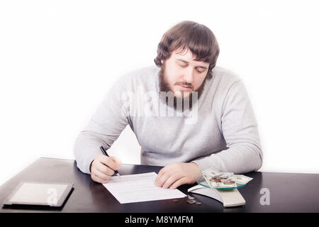 A handsome young programmer, working, dreaming, at the table, looking at the money, coming up with the creation of a new program. Stock Photo