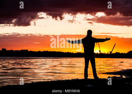 Happy celebrating winning success woman at sunset or sunrise standing elated Stock Photo