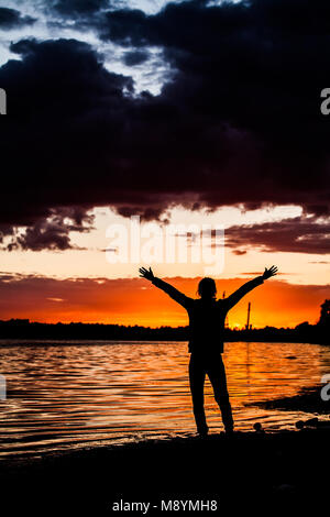 Silhouette of a man standing on a tree stump in the shore break of a beach Stock Photo